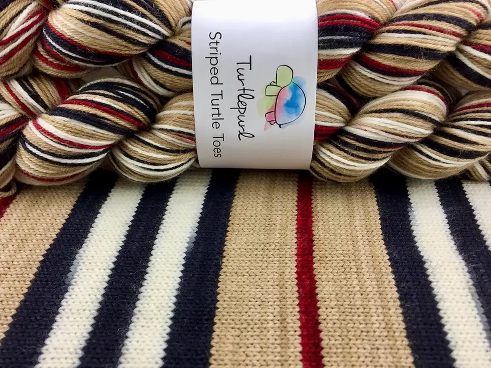 Skeins of striped yarn in beige, red, black, and white are placed on a matching knitted fabric. Label reads "Turtlepurl Striped Turtle Toes."