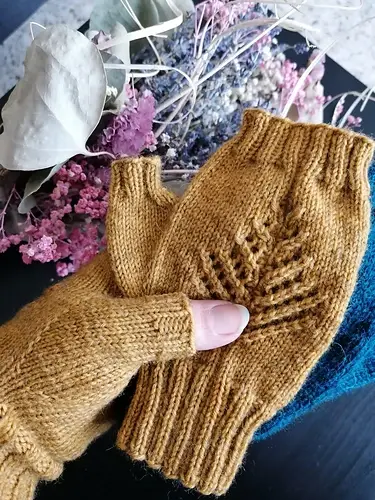 Yellow knit fingerless gloves held in hand over a table with pink and white dried flowers, creating a cozy and warm atmosphere.