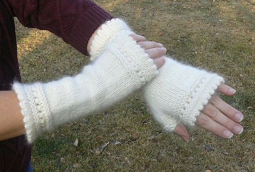 Hands wearing white knitted fingerless gloves on a grass background. One arm is crossed over the other. Cozy and warm atmosphere.