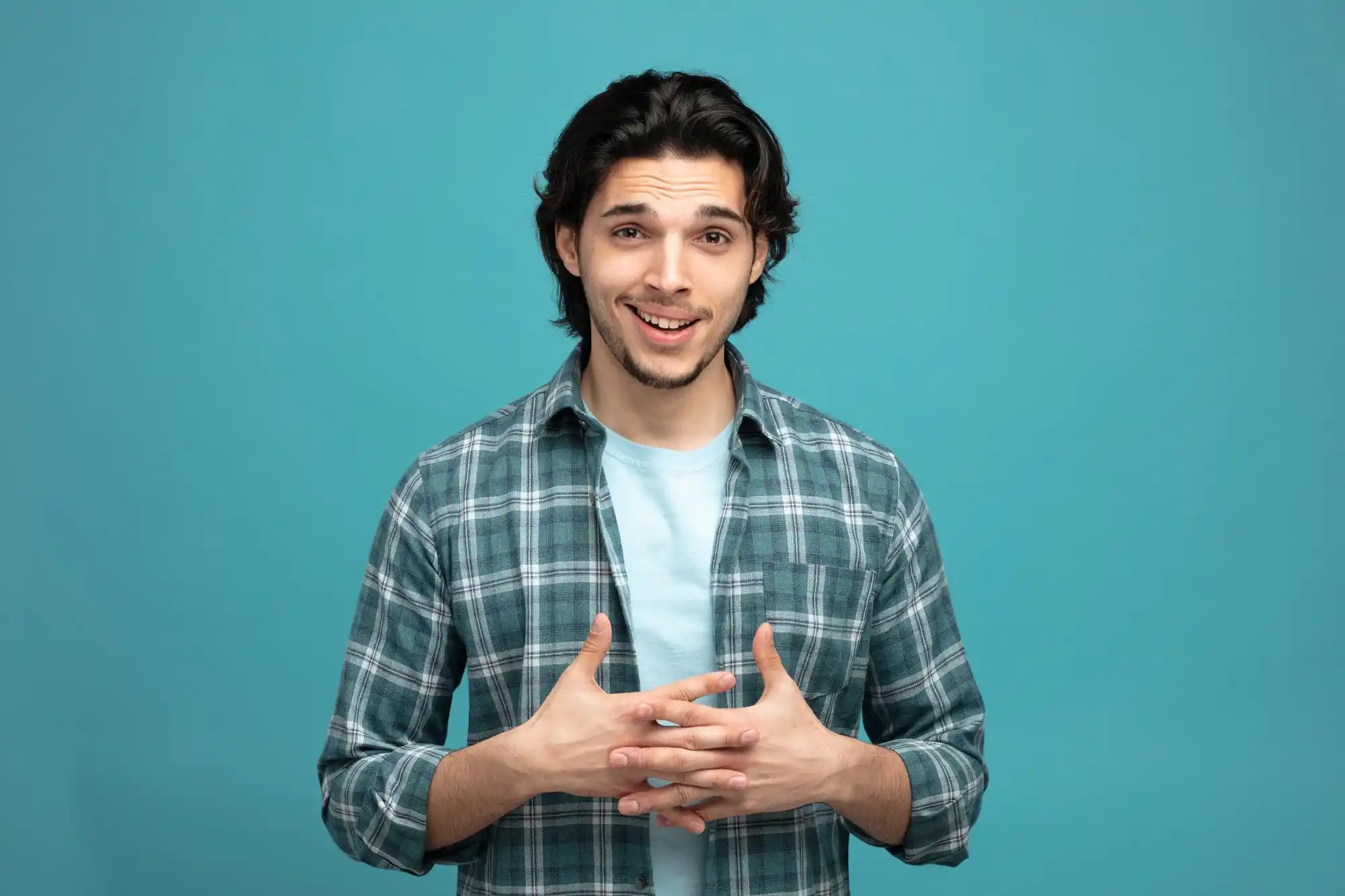 Young man smiling, hands clasped, wearing plaid shirt against blue background.