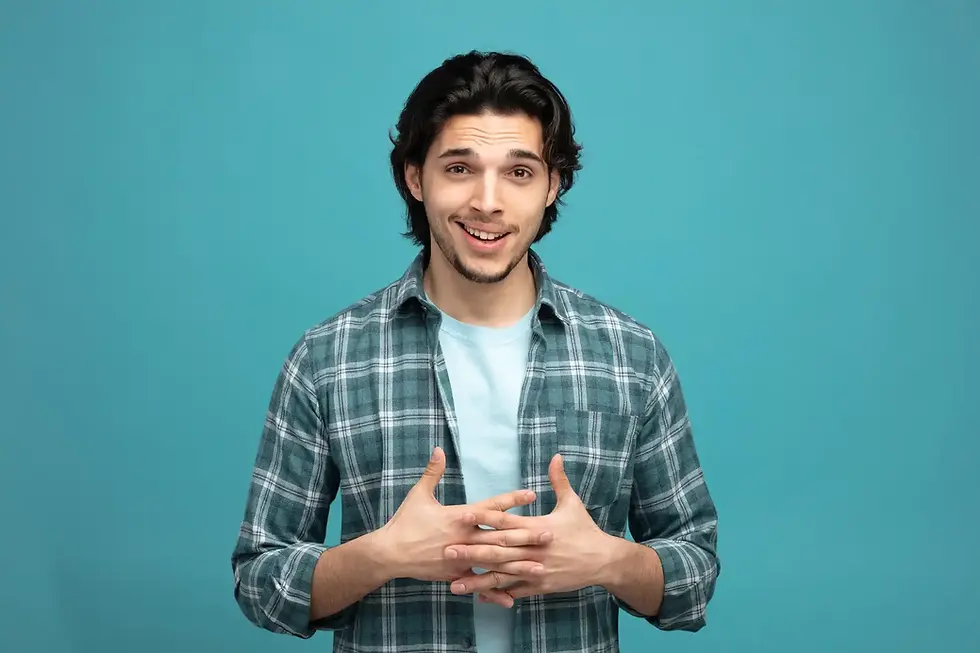 Young man in plaid shirt smiling, hands clasped, teal background.