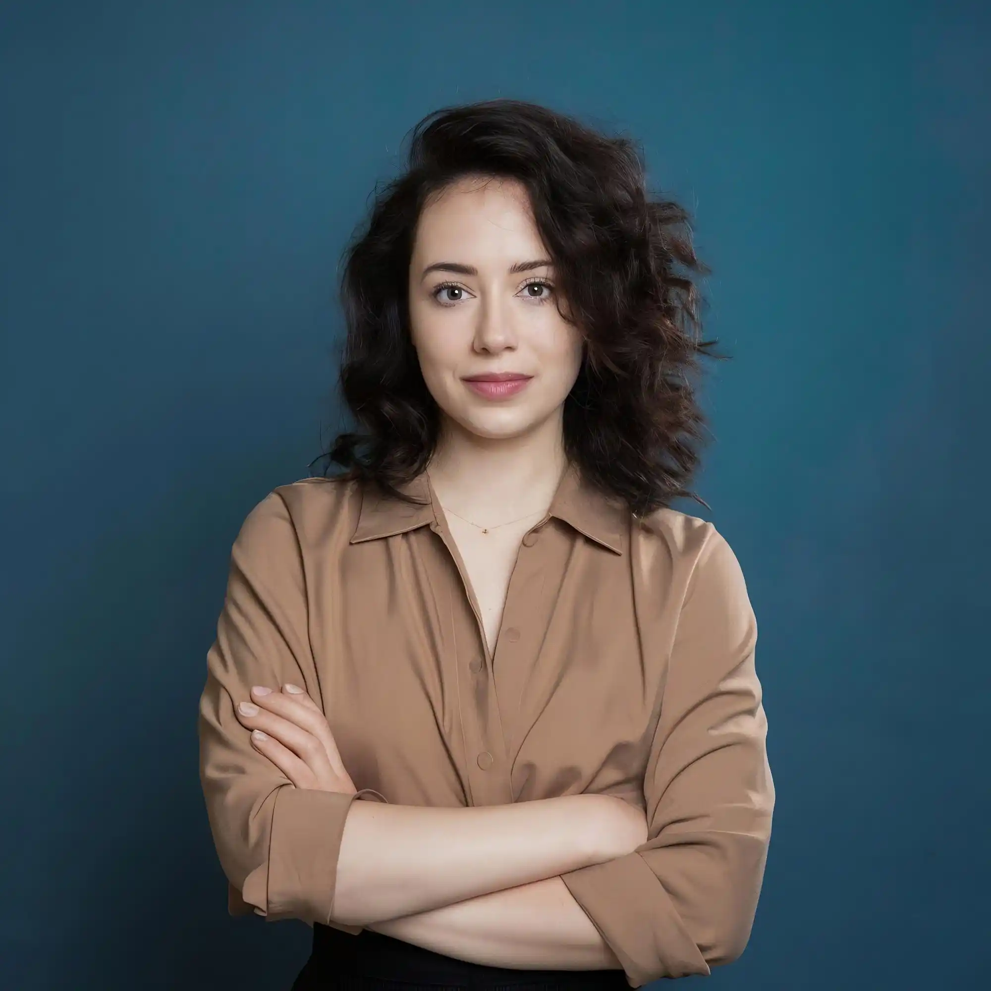 Young woman with dark curly hair, arms crossed, smiling confidently.
