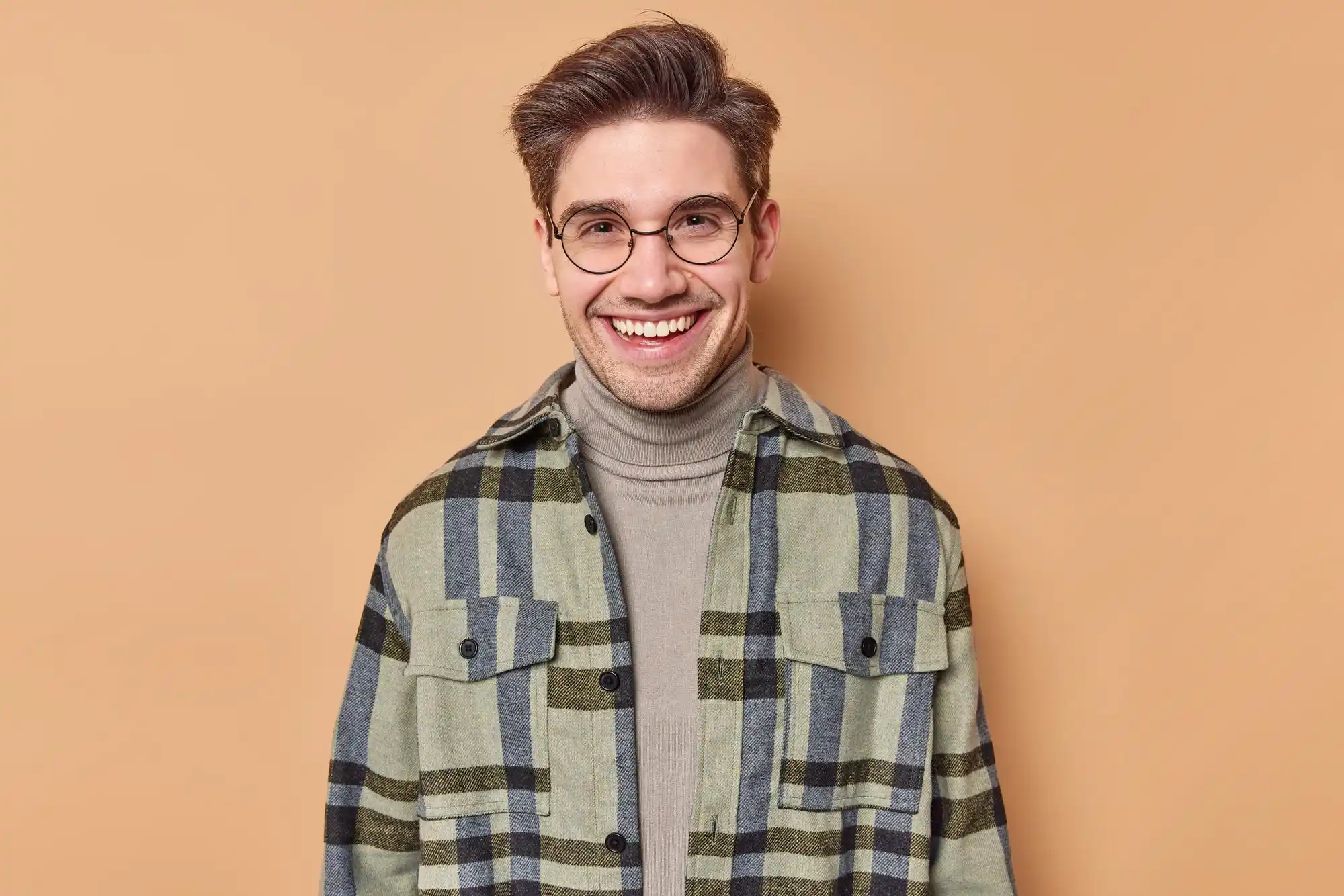 Smiling man in plaid shirt and glasses against a beige background.