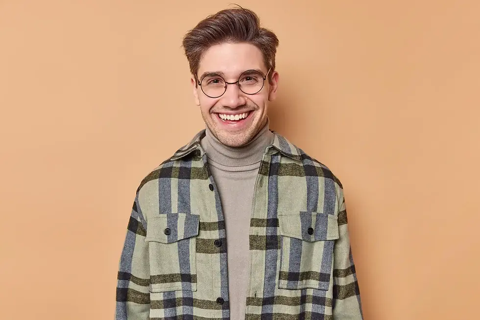 Young man smiling, wearing glasses and plaid shirt against beige background.