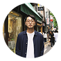 Man with glasses standing on a busy city street in front of shops.