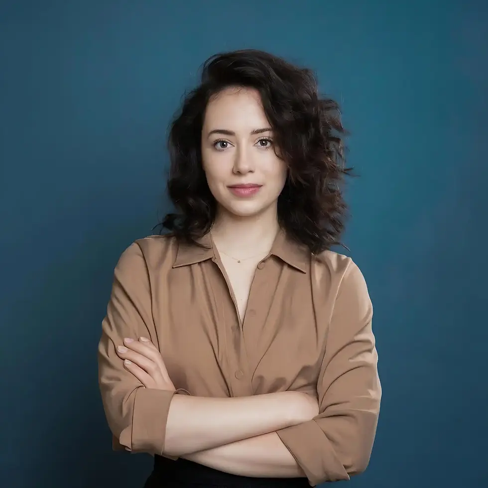 Woman with curly hair, brown shirt, arms crossed against a blue background.