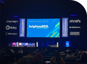 Audience at brightonSEO event with a blue stage backdrop. Text on screen: "brightonSEO, 30 April & 1 May 2026, United Kingdom."