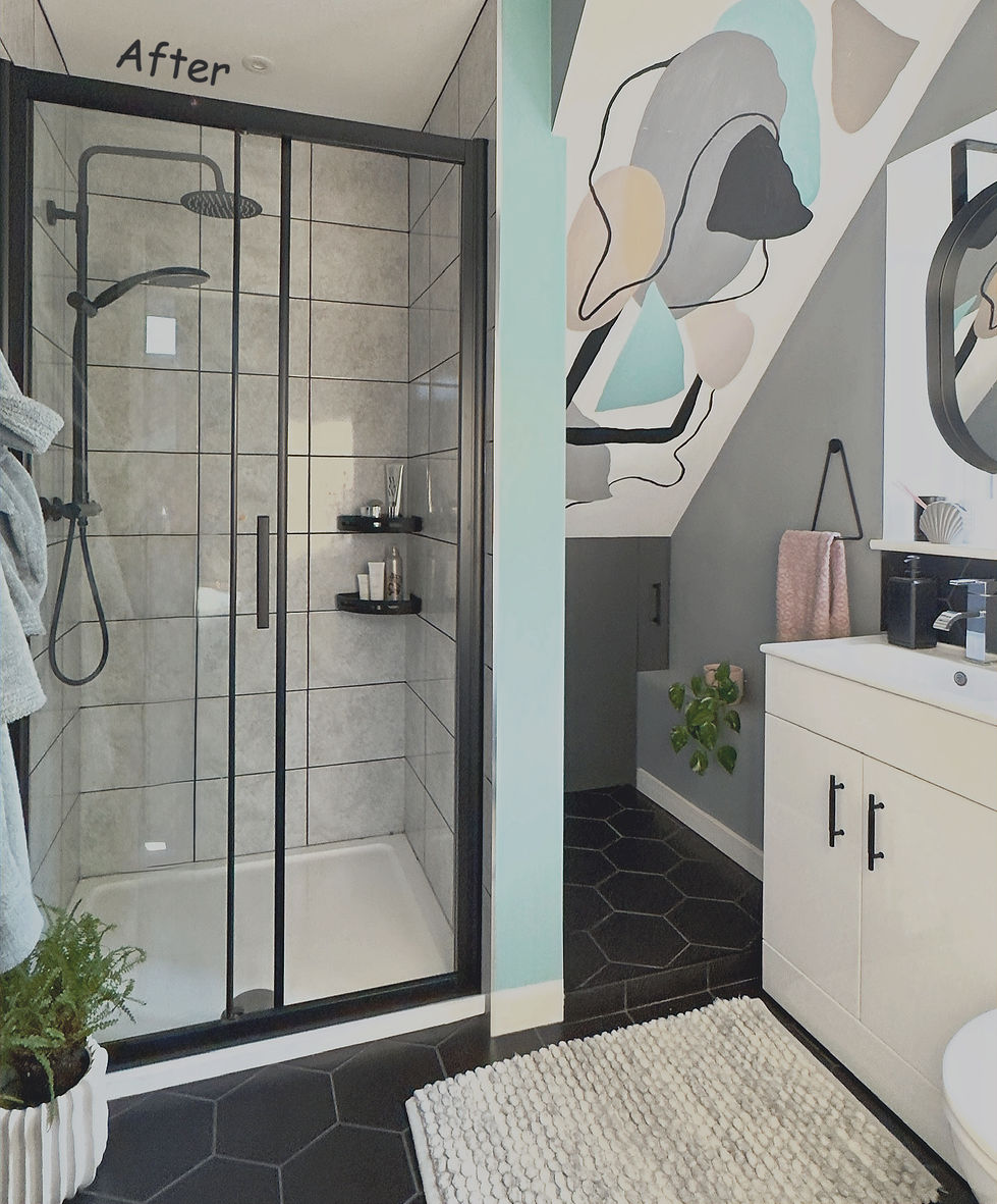 A contemporary bathroom with a black-framed walk-in shower featuring large light grey wall tiles, a rainfall shower head, and built-in corner shelves. Black hexagonal floor tiles create a bold contrast with the white shower tray and vanity unit. Beside the shower, a feature wall displays an abstract mural in soft grey, beige, black, and aqua tones beneath a sloped ceiling. A white vanity with black handles provides storage, while a white textured bath mat, a potted trailing plant, and neatly arranged accessories add warmth and a modern, stylish finish.
