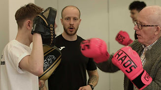 Coach supporting gentleman hitting boxing pads