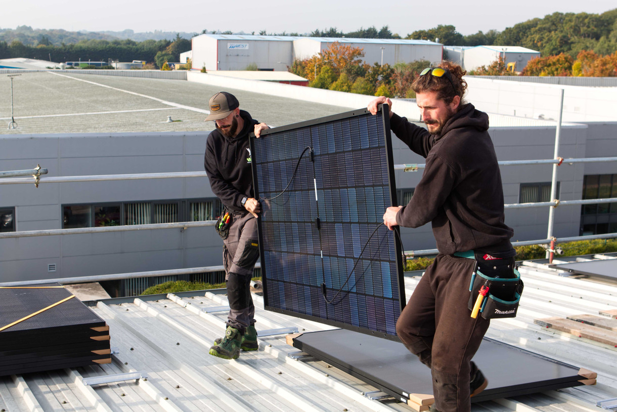 2 Electricians carrying solar panels into position on the roof.