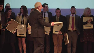 Older man handing out awards on stage at conference