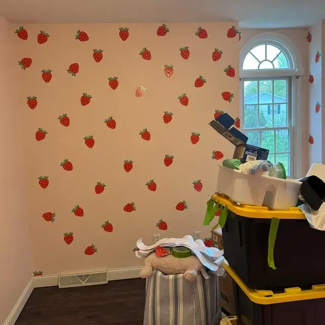 Verspielte Erdbeer-Wandaufkleber, die eine süße Akzentwand in einem Kinderzimmer mit hellrosa Farbe für ein frisches, fruchtiges Raumthema schaffen.