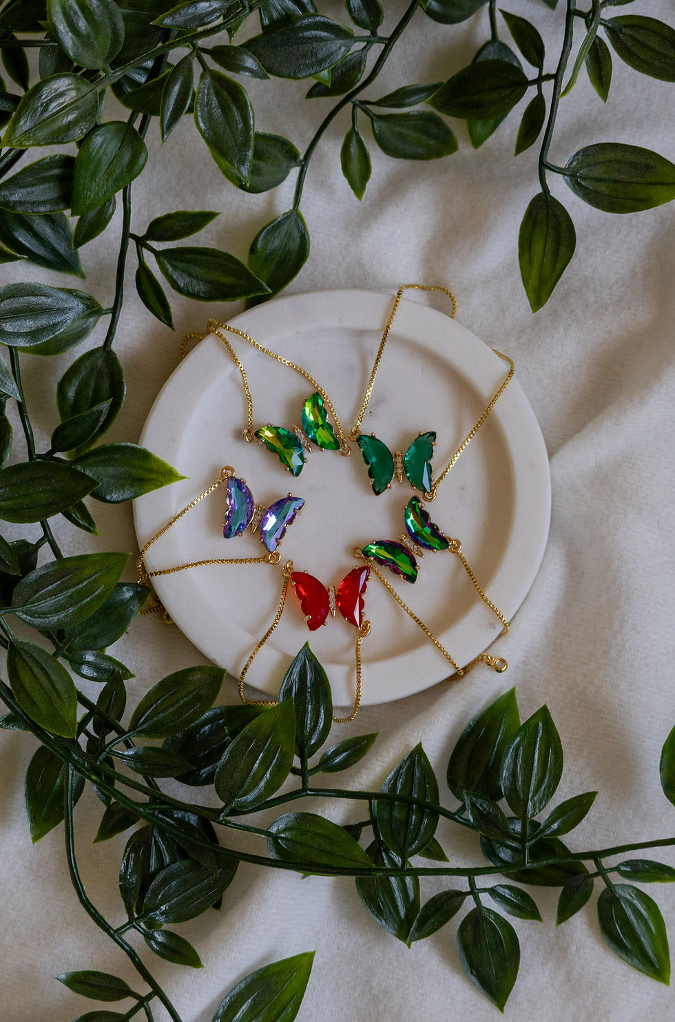 Thumbnail: Spring Glimmer Butterfly necklaces in various colors on a white plate.