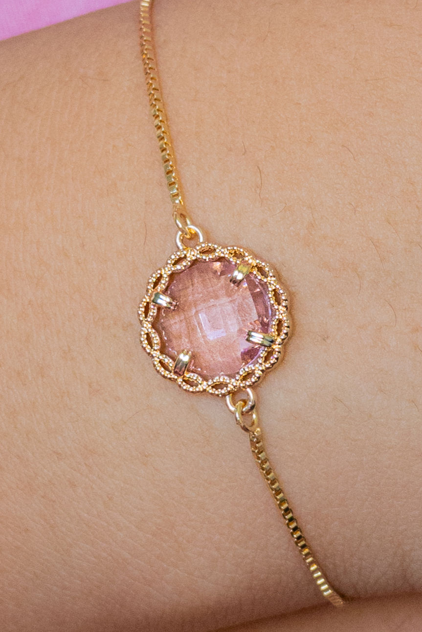 Closeup of a bracelet with a pink gemstone and a gold chain