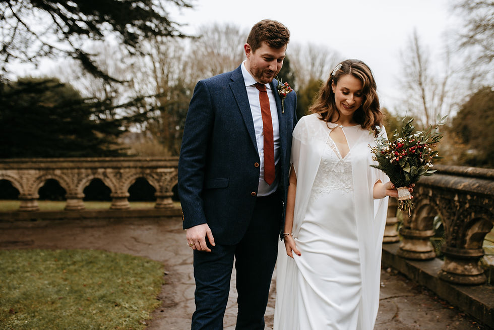 A joyful couple strolls through a picturesque garden setting, with the bride holding a vibrant bouquet and the groom in a sharp suit, capturing a moment of happiness on their special day.