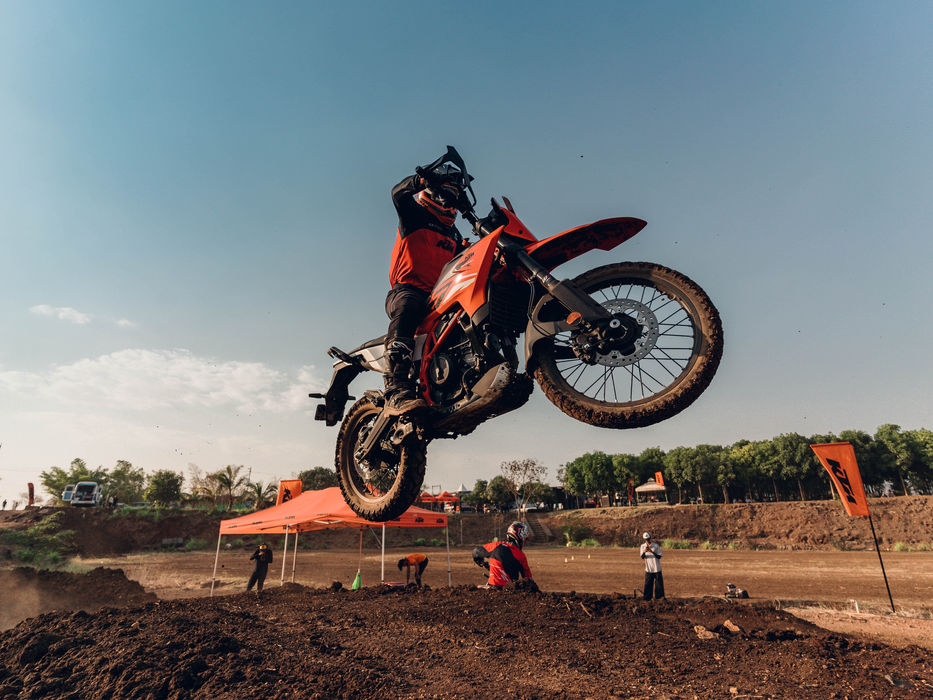 A motorcycle racer jumps over a dirt hill in a motocross competition.