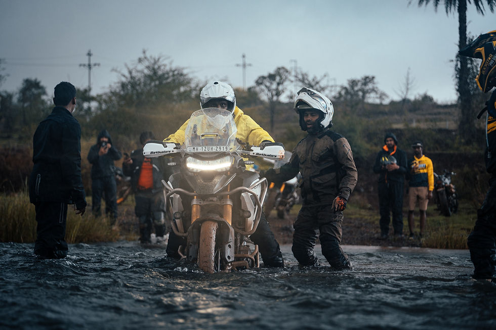 Motorcyclist rides motorcycle through water with help from others in the background