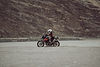 Motorcyclist riding across the desert landscape, wearing a helmet and riding gear.