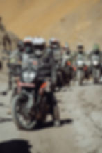 Motorcyclists riding on a dirt road through mountainous terrain; adventure trip, outdoors.