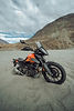 Orange motorcycle parked on sand with a mountain range in the background Nelly.