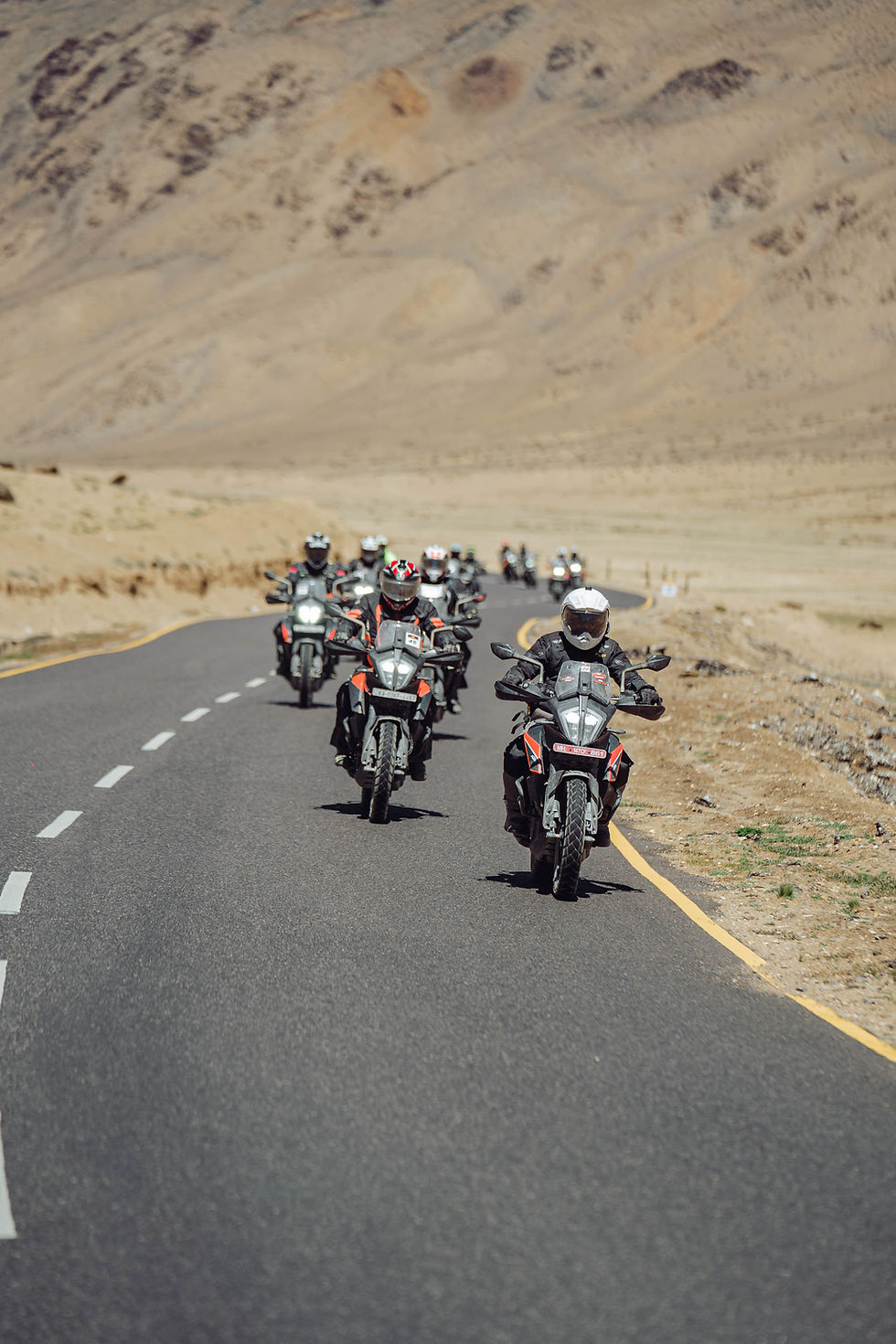 Group of motorcyclists riding down a winding road in a desert with mountains.