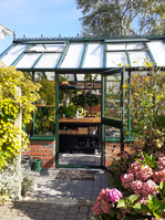 Midsize glasshouse on a low wall with open turning door on the side and Victorian ridge decoration