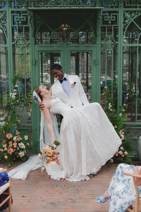 A bride gets dipped by her groom outside a gorgeous emerald green venue