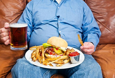 Overweight male sitting on the couch with large plate of food on his lap