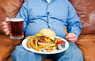 overweight male sitting on the couch with a large plate of food on his lap