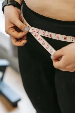 Woman using tape measure around waist, measuring progress in black leggings.
