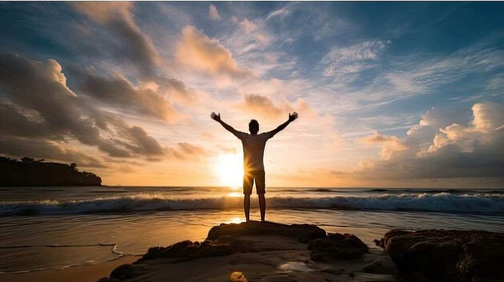 Man with arms wide open, standing on rock ledge at the beach during sunset