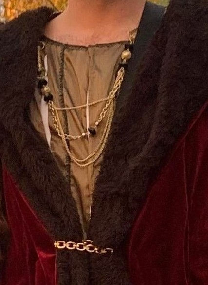 Détail de costume François 1er en velours rouge et fausse fourrure noire sur fond de gilet doré avec chaines