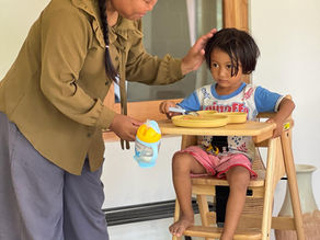 Local caregiver feeding a child in a rented high chair in Lombok, perfect for traveling families needing baby gear