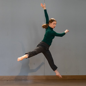 Robyn Pilecki performing a sissone a la second. She is looking towards the down stage left corner of the stage and her torso is twisting to the right with the help of her hands.