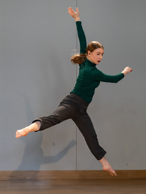 Robyn Pilecki performing a sissone a la second. She is looking towards the down stage left corner of the stage and her torso is twisting to the right with the help of her hands.