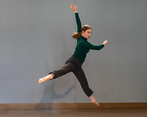 Robyn Pilecki performing a sissone a la second. She is looking towards the down stage left corner of the stage and her torso is twisting to the right with the help of her hands.