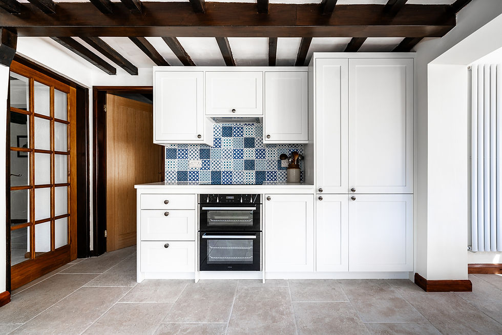 Traditional bespoke fitted kitchen in Derby with white shaker cabinets, patterned blue tile splashback, exposed beams, and integrated double oven by Duffield Kitchens.