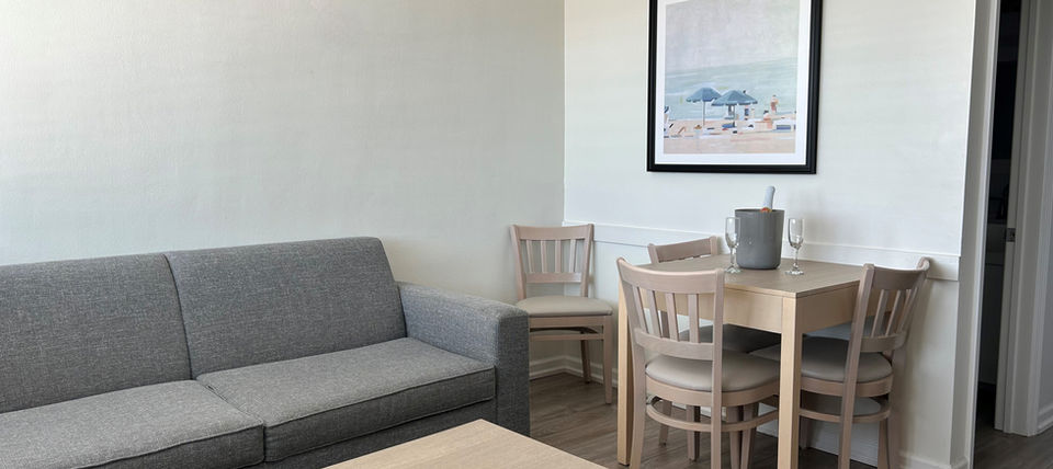 Bright living area with gray sofa, wooden dining set, beach art.