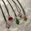 Thumbnail: Five stained glass necklaces -  three trees, two mushrooms - with leather straps on a white cushion