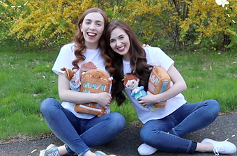 Present-Day Caroline and Katherine holding Bibli Plushies and wearing their "Always Be Your-Shelf" T-shirts.