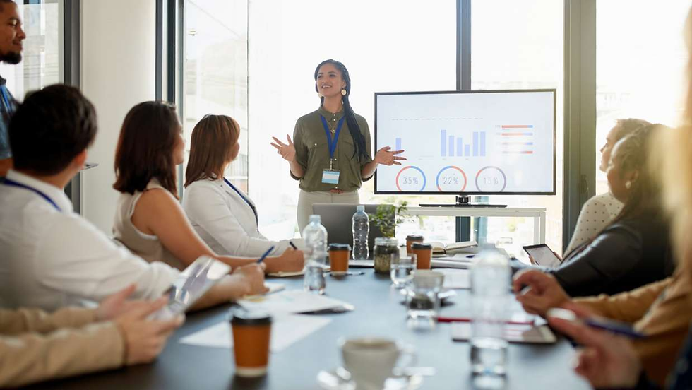 Woman presents bar charts on a screen to a conference room of seated coworkers, in a bright office meeting, engaged and focused