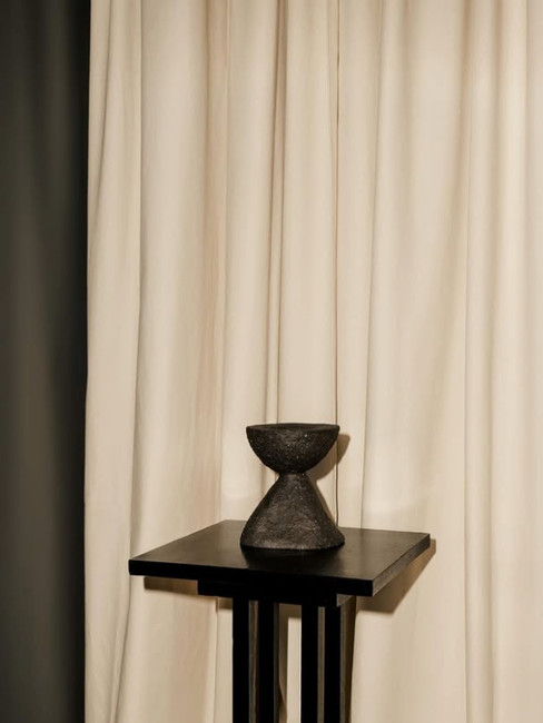 Studio par Agata Melerska, avec guéridon noir, objet sculptural et rideaux clairs.