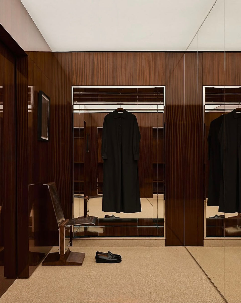 Dressing en bois sombre, jeu de miroirs et manteau noir suspendu dans la lumière.