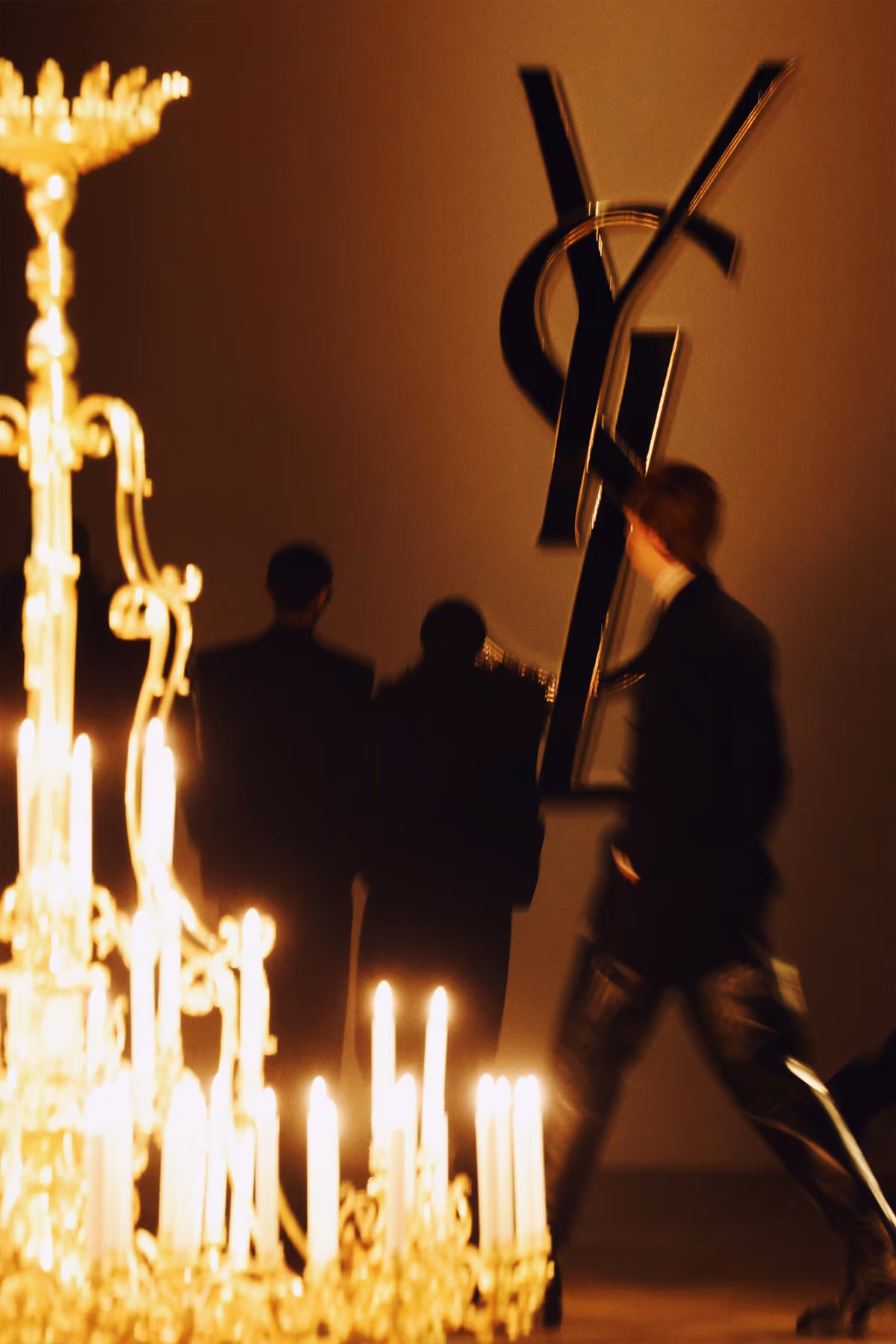 Saint Laurent Men’s Winter 2025 fashion show, with models moving among golden chandeliers.
