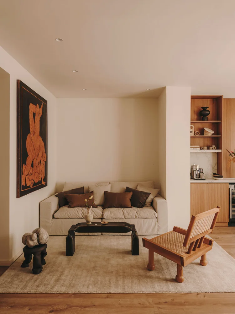 Living room of Arcadia by Santa Living and MA&Partners, with a light sofa, wooden armchair, black coffee table and wall artwork.