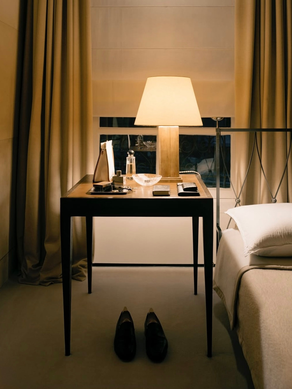 Chambre parisienne aux tons sable, rideaux pleins et lumière douce sur table de chevet.