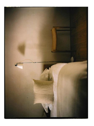 Bedroom interior by Maureen M. Evans for Architectural Digest — minimalist bed, soft pillow, wicker chair.