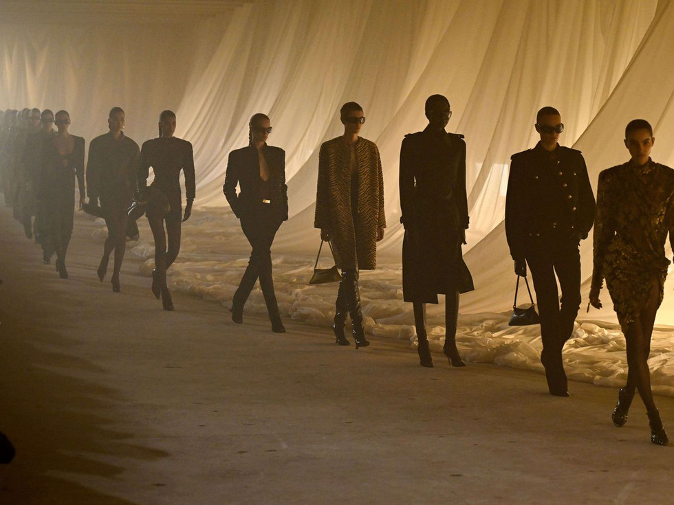 Balmain Autumn/Winter 2026 fashion show, with models walking between translucent veils lit with golden light.