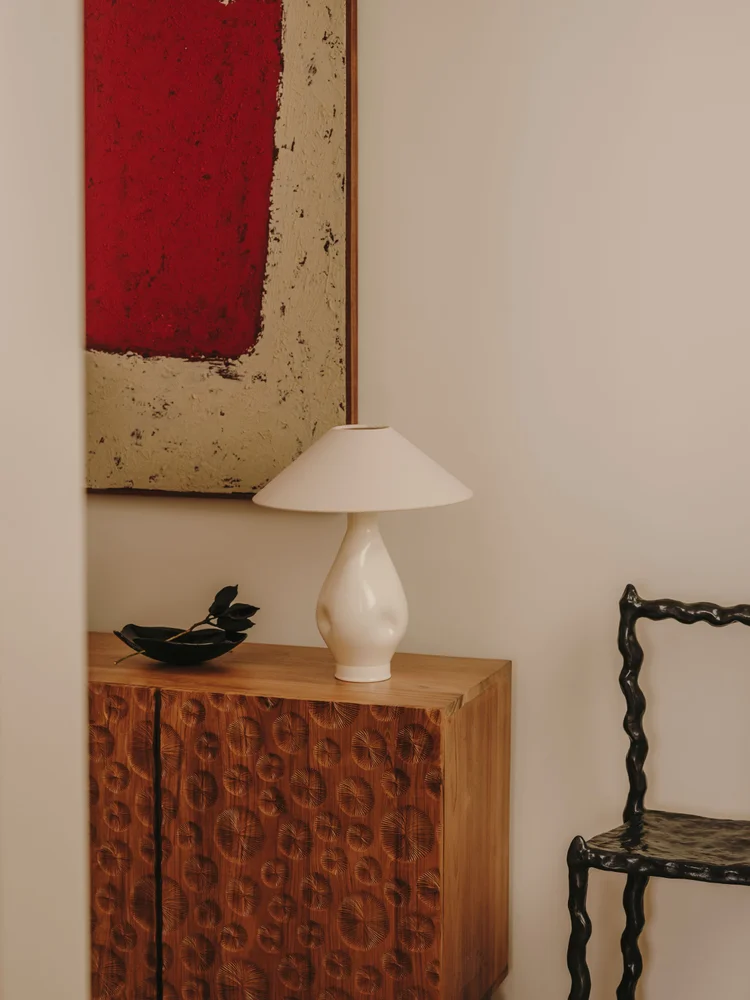 Detail of Arcadia by Santa Living and MA&Partners, with a sculptural wooden cabinet, white lamp, red artwork and black chair.