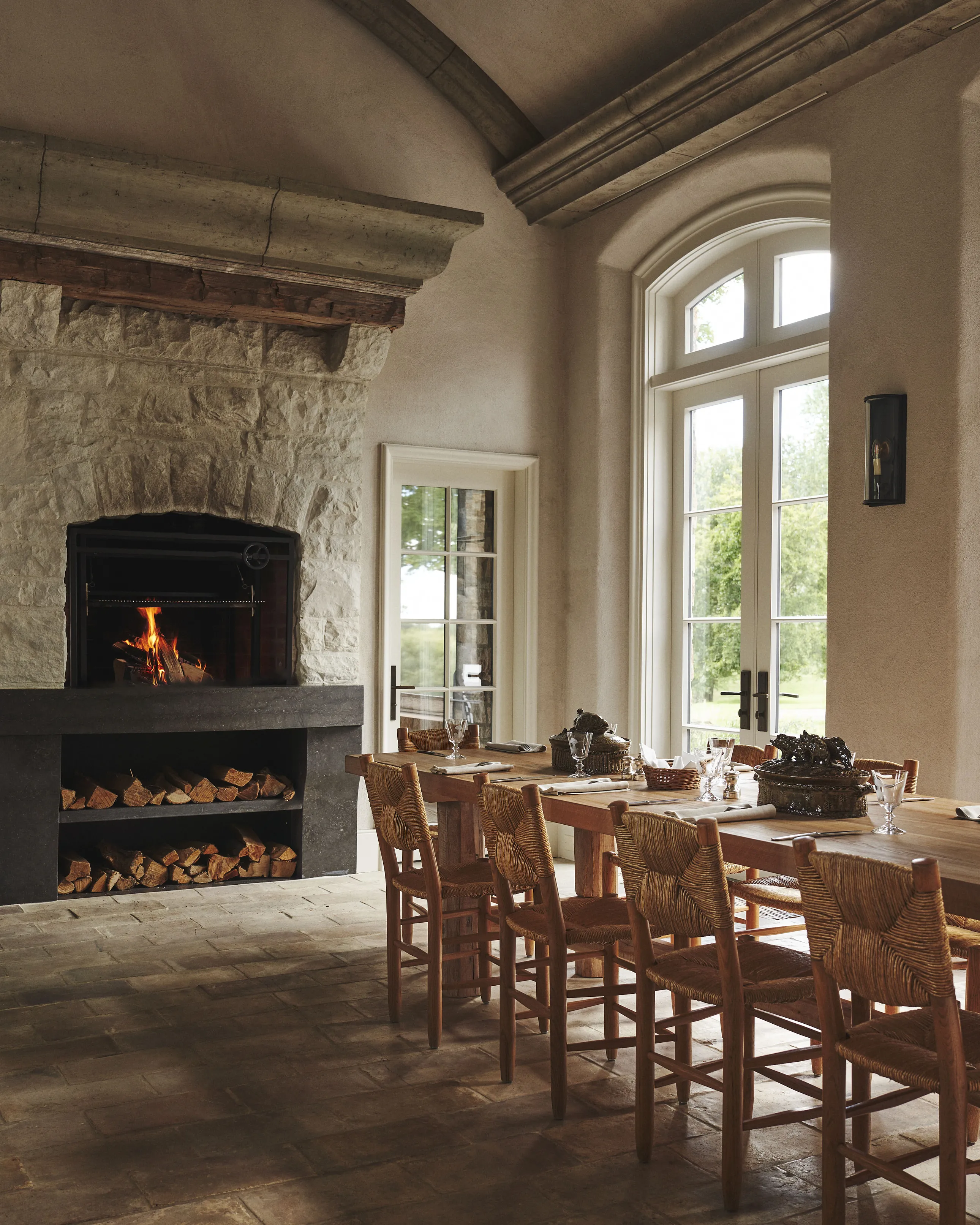 Salle à manger rustique, cheminée en pierre, table en bois et chaises tressées.